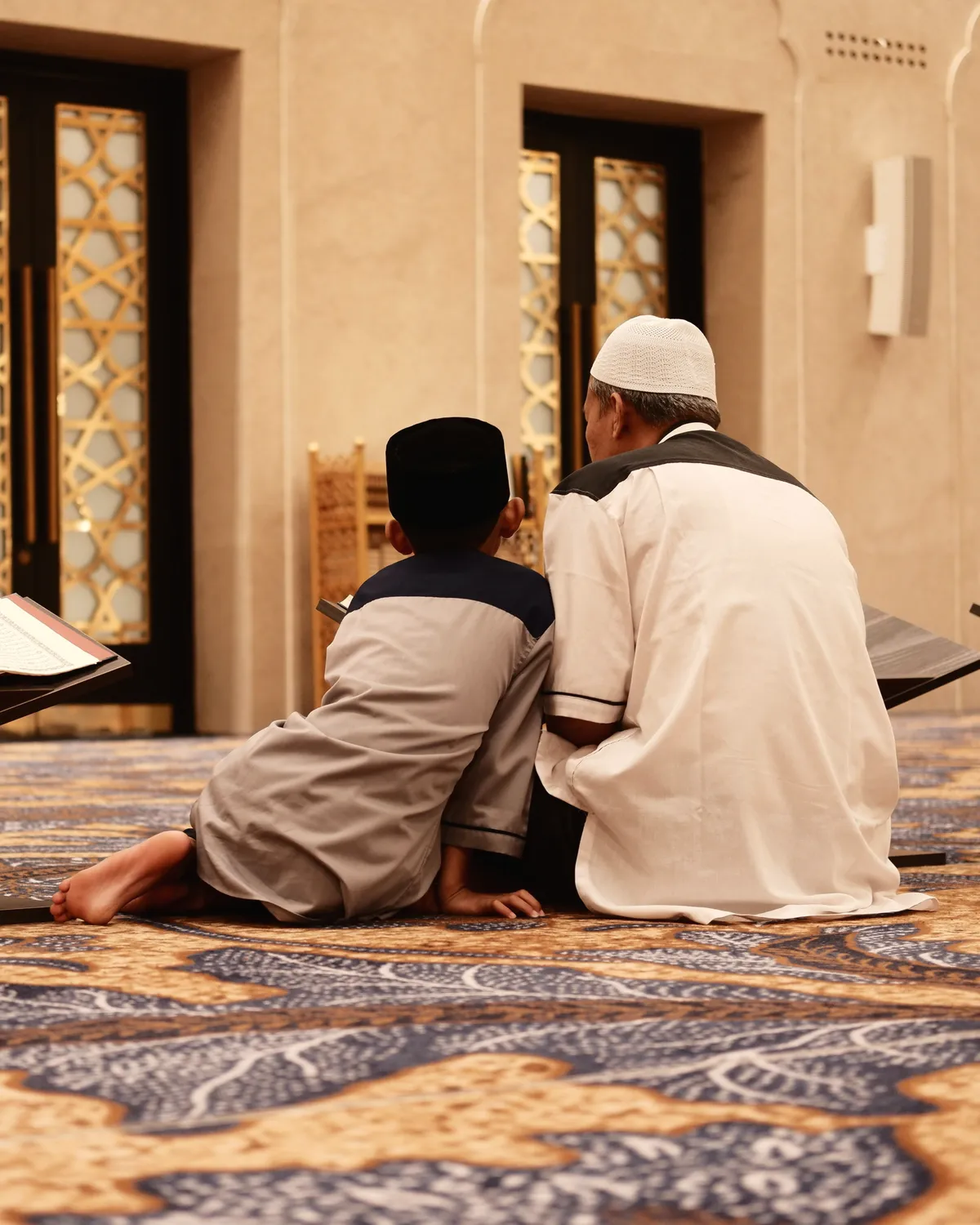 Teacher and young student sitting side by side reading the Quran in a mosque