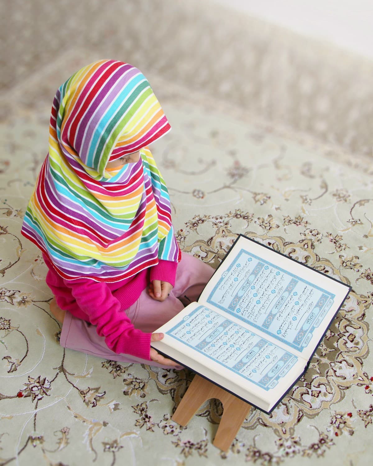 Young student in a colourful hijab reading the Quran at home