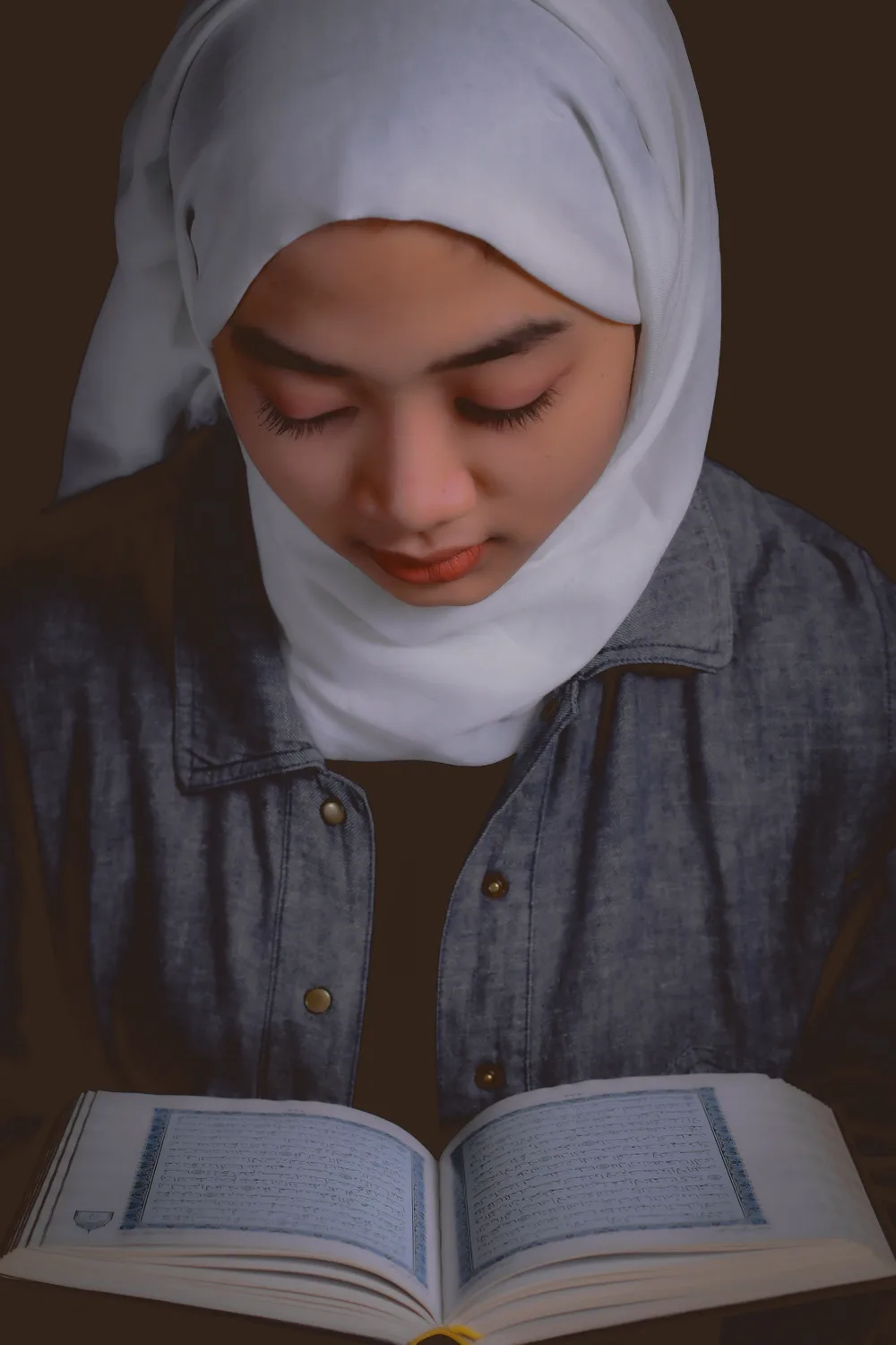 Young woman in a white hijab quietly reading the Quran
