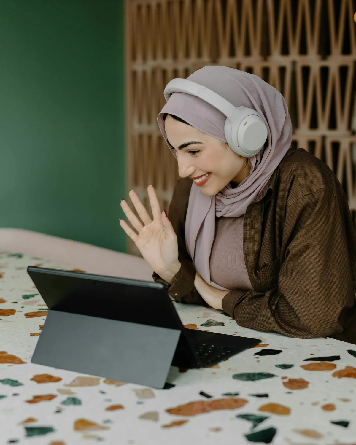 Smiling female Quran teacher waving hello to a student during an online lesson